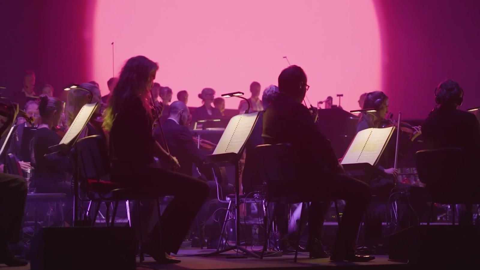 Sonic branding for events: an orchestra plays on stage in front of a pink-lit screen at a Cinema in Concert show