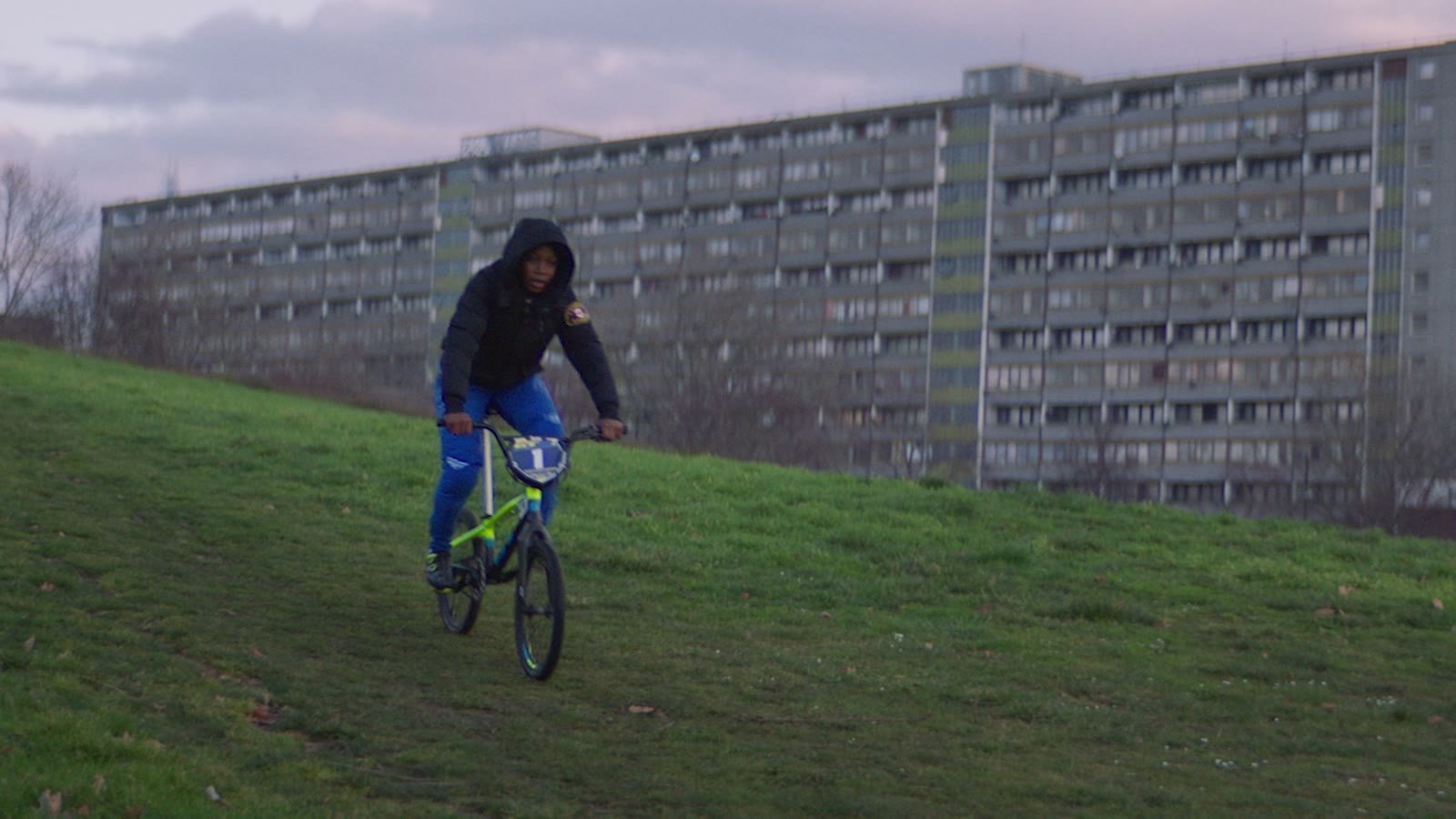 Sonic branding for nonprofits: a young rider on a BMX bike crossing the grass in front of a council estate in Peckham, London