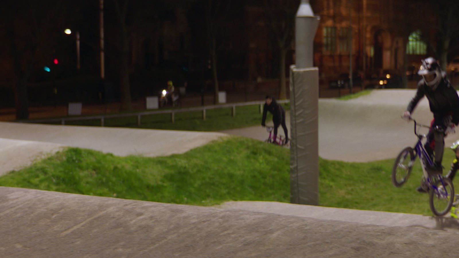 Sonic branding for sports brands: two BMX riders in full-face helmets jump on a pump track at night in Peckham, London